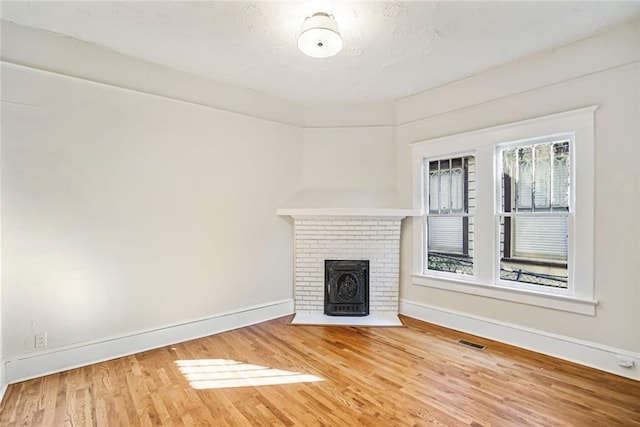 unfurnished living room featuring visible vents, a fireplace, baseboards, and wood finished floors