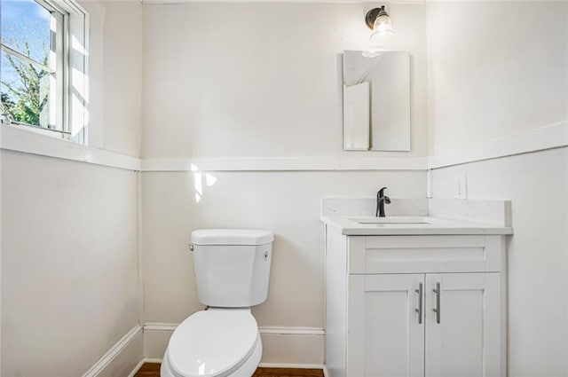 half bathroom featuring toilet, vanity, and baseboards