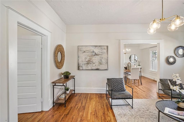 sitting room featuring a chandelier, a textured ceiling, wood finished floors, and baseboards