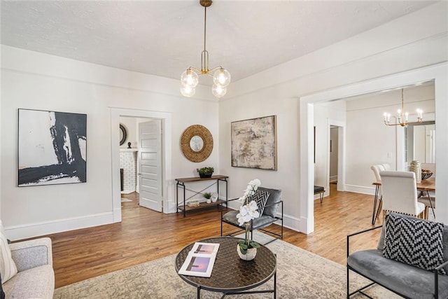 living area with baseboards, a textured ceiling, wood finished floors, and a notable chandelier