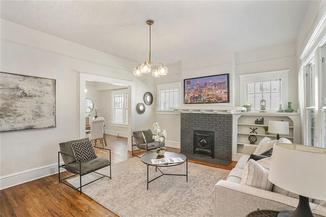 living area featuring a notable chandelier, a fireplace, baseboards, and wood finished floors