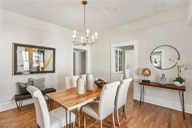 dining area featuring light wood-style floors, a notable chandelier, a textured ceiling, and baseboards