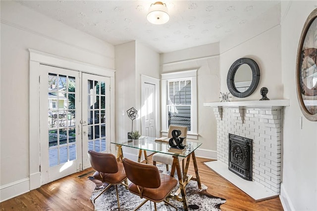 dining space with a brick fireplace, french doors, baseboards, and wood finished floors