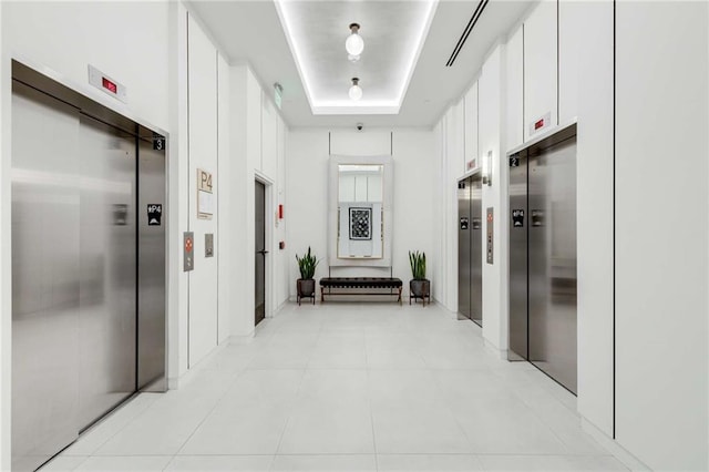 hallway with light tile patterned floors, elevator, and a tray ceiling