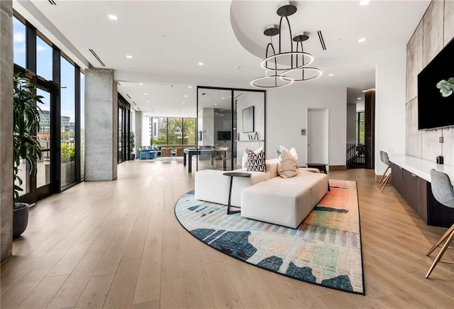 living area with light wood-style floors, recessed lighting, a chandelier, and a wall of windows