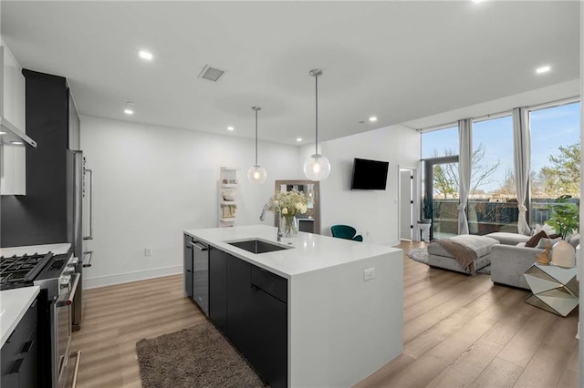 kitchen featuring appliances with stainless steel finishes, a sink, light countertops, dark cabinetry, and recessed lighting