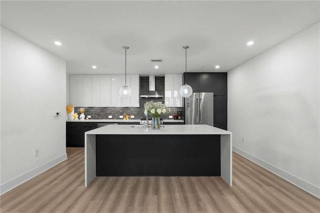 kitchen with freestanding refrigerator, light countertops, decorative backsplash, and wall chimney exhaust hood