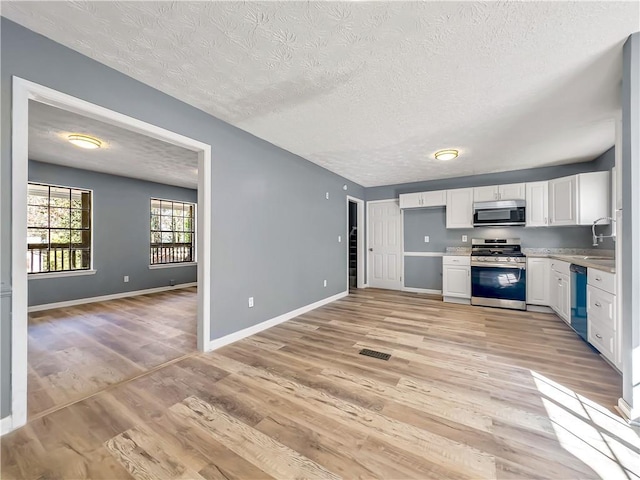 kitchen featuring stainless steel appliances, white cabinetry, a textured ceiling, and light hardwood / wood-style flooring