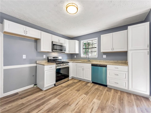 kitchen featuring stainless steel appliances, a textured ceiling, white cabinets, light hardwood / wood-style flooring, and sink