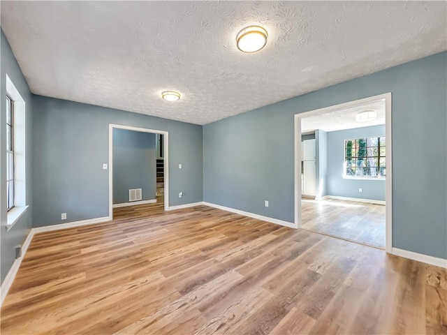 empty room with a textured ceiling and light hardwood / wood-style floors