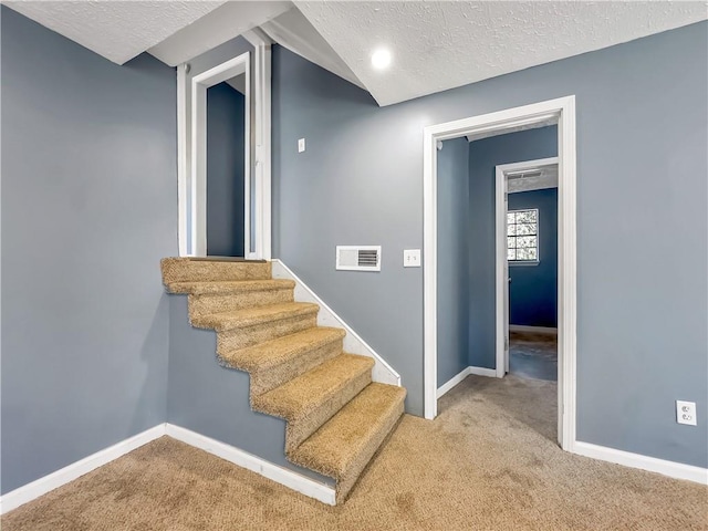 stairs featuring a textured ceiling and carpet