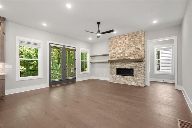 unfurnished living room featuring recessed lighting, dark wood finished floors, french doors, and a stone fireplace