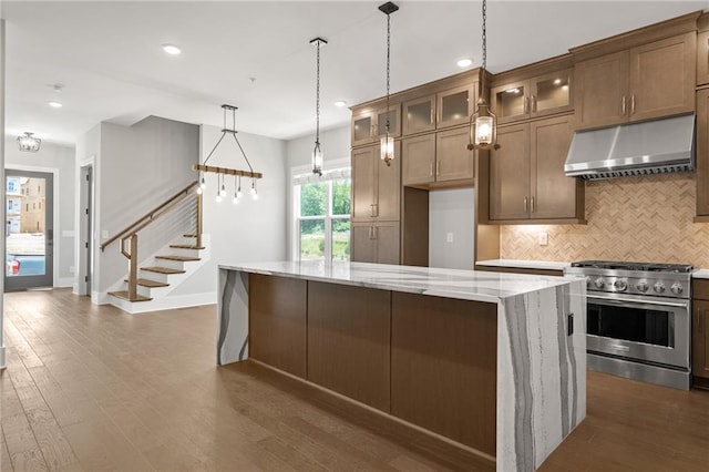 kitchen featuring light stone counters, under cabinet range hood, high end stainless steel range, backsplash, and dark wood finished floors