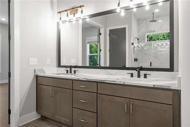 full bathroom with baseboards, a sink, a marble finish shower, and double vanity