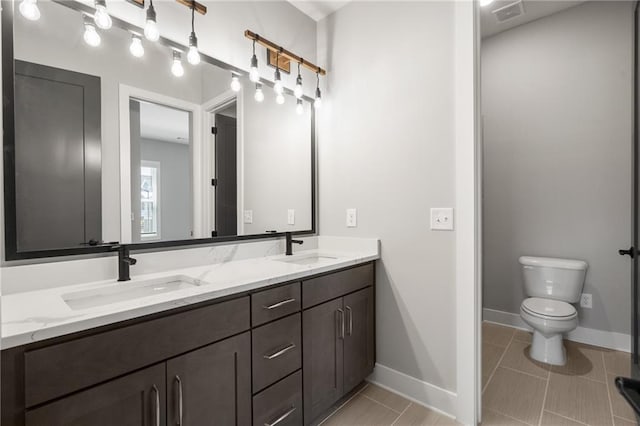 bathroom featuring toilet, double vanity, visible vents, and a sink