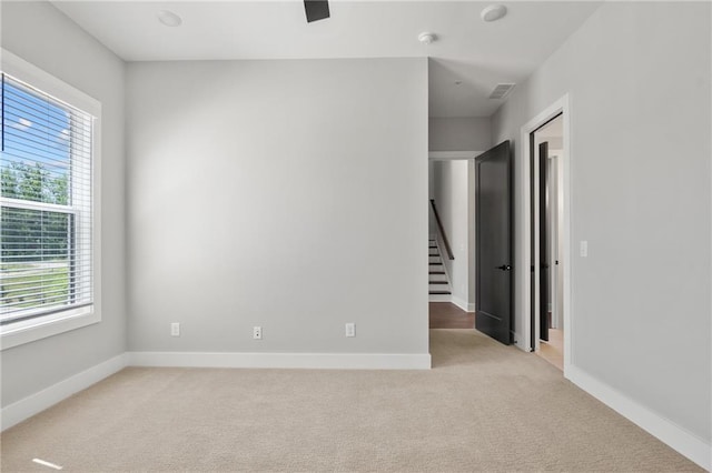 unfurnished room featuring light colored carpet, visible vents, baseboards, and stairs