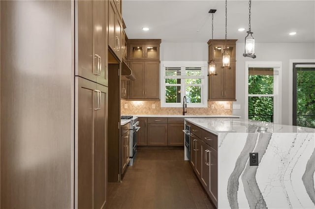 kitchen with a sink, wall chimney range hood, decorative backsplash, high end range, and light stone countertops