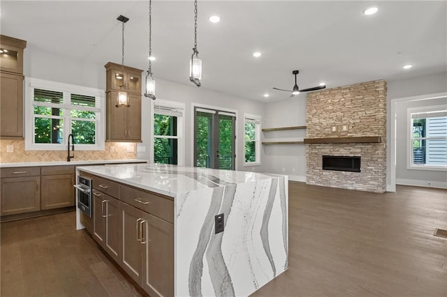 kitchen featuring a stone fireplace, light stone counters, dark wood-type flooring, backsplash, and a center island