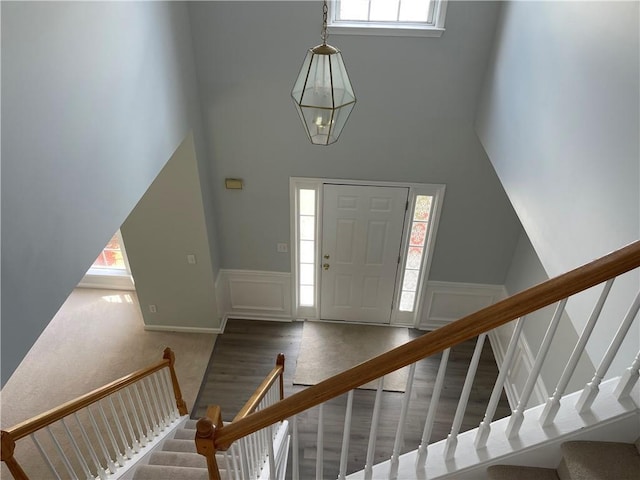 carpeted foyer entrance with stairs, a high ceiling, wainscoting, a decorative wall, and a chandelier