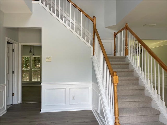 stairway with wood finished floors, a decorative wall, a towering ceiling, and a wainscoted wall