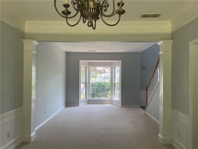 spare room featuring carpet flooring, stairway, a chandelier, crown molding, and decorative columns
