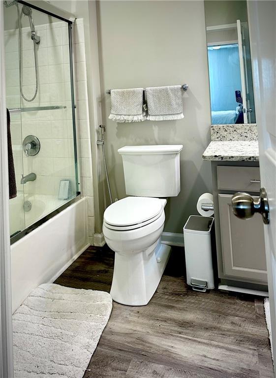 full bathroom with toilet, wood finished floors, baseboards, combined bath / shower with glass door, and vanity