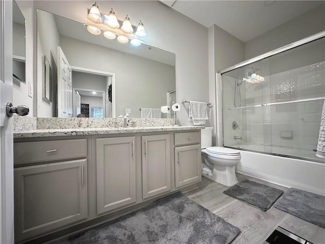 full bath featuring toilet, vanity, bath / shower combo with glass door, and wood finished floors