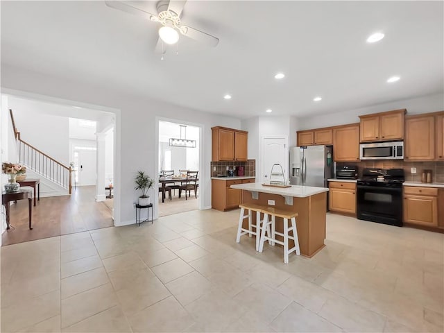 kitchen featuring a breakfast bar area, a kitchen island with sink, stainless steel appliances, light countertops, and backsplash