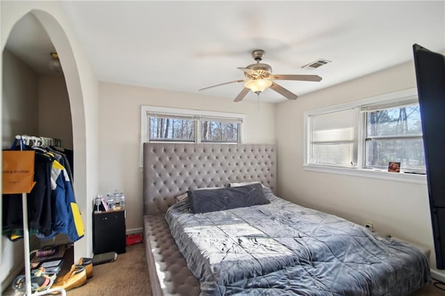 carpeted bedroom featuring arched walkways, multiple windows, ceiling fan, and visible vents