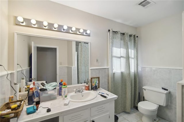 bathroom featuring a wainscoted wall, toilet, visible vents, and tile walls