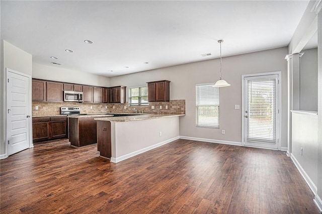 kitchen with kitchen peninsula, tasteful backsplash, appliances with stainless steel finishes, decorative light fixtures, and dark wood-type flooring