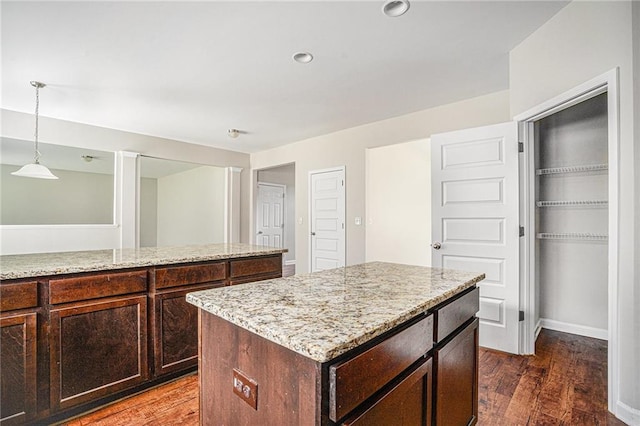 kitchen with dark wood-type flooring, pendant lighting, light stone counters, and a center island