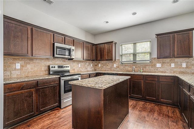 kitchen with stainless steel appliances, light stone counters, dark hardwood / wood-style floors, backsplash, and a center island