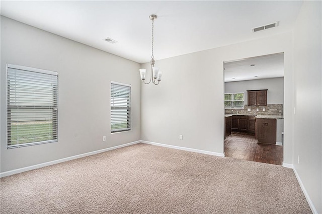 carpeted empty room featuring a chandelier and plenty of natural light