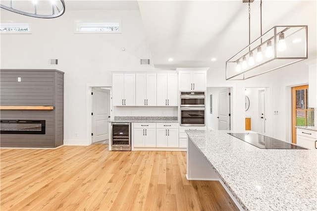 kitchen featuring double oven, white cabinets, beverage cooler, hanging light fixtures, and black electric stovetop