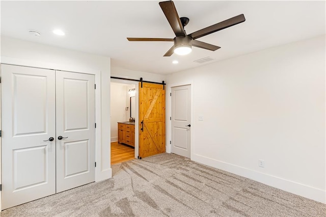 unfurnished bedroom with ensuite bathroom, ceiling fan, a barn door, light carpet, and a closet