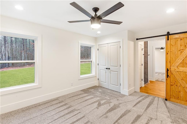 unfurnished bedroom with a barn door, light colored carpet, ceiling fan, and a closet