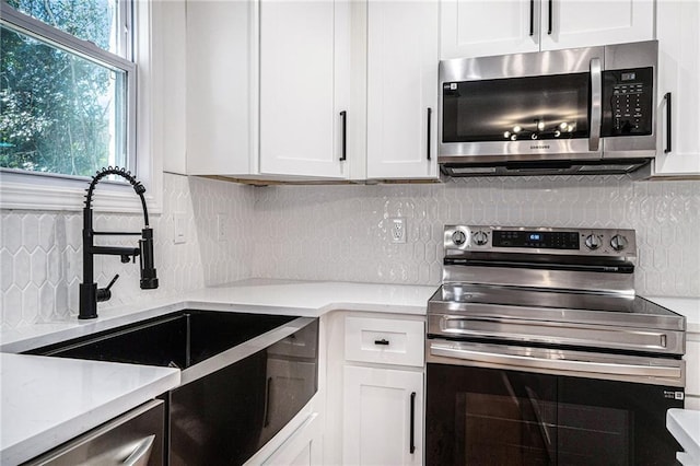 kitchen featuring white cabinets, backsplash, appliances with stainless steel finishes, and sink