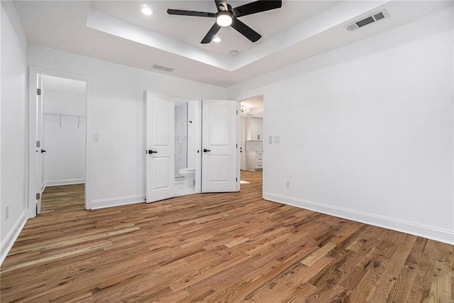 unfurnished bedroom with ceiling fan, hardwood / wood-style flooring, a tray ceiling, and a walk in closet