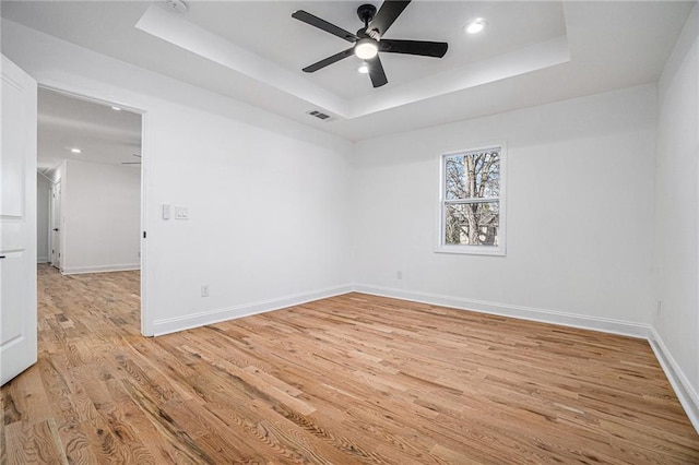 spare room with ceiling fan, light hardwood / wood-style flooring, and a tray ceiling