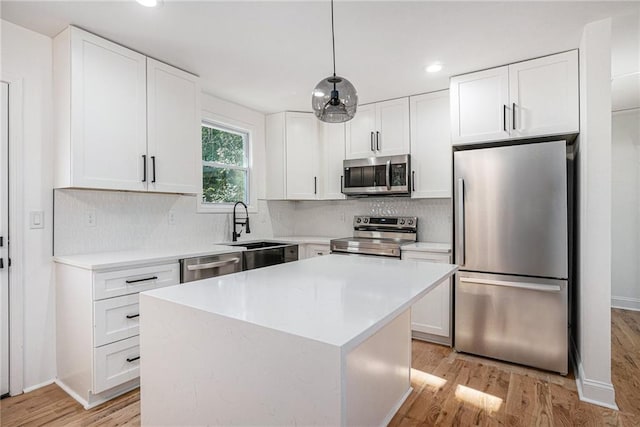 kitchen featuring pendant lighting, white cabinets, a center island, stainless steel appliances, and light hardwood / wood-style floors