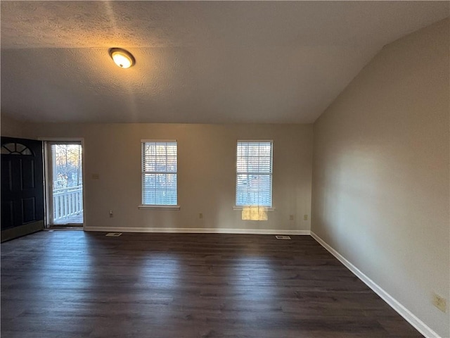 empty room with dark wood-type flooring, a textured ceiling, and vaulted ceiling