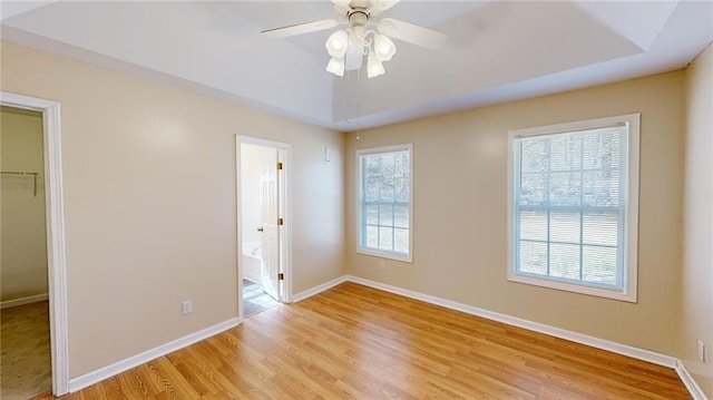 unfurnished bedroom with ceiling fan, ensuite bathroom, a raised ceiling, a spacious closet, and a closet