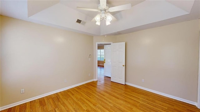 empty room with ceiling fan, light hardwood / wood-style flooring, and a tray ceiling