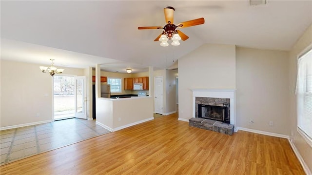 unfurnished living room featuring light wood-type flooring, ceiling fan with notable chandelier, a stone fireplace, and lofted ceiling