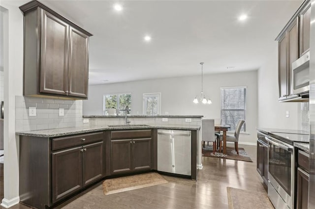 kitchen featuring sink, hanging light fixtures, light stone counters, kitchen peninsula, and stainless steel appliances