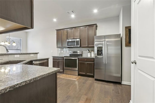 kitchen with appliances with stainless steel finishes, sink, dark brown cabinets, light stone counters, and dark wood-type flooring