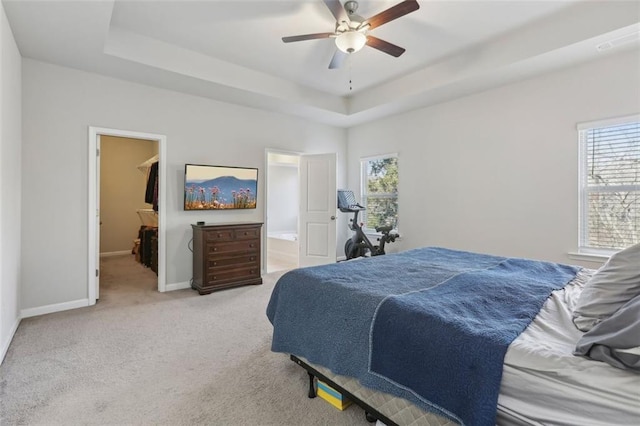 carpeted bedroom featuring ceiling fan, a walk in closet, a raised ceiling, and ensuite bath