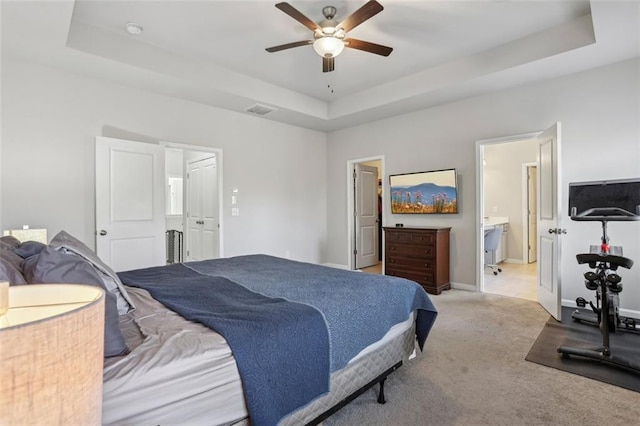 bedroom featuring a raised ceiling, light colored carpet, and ensuite bath