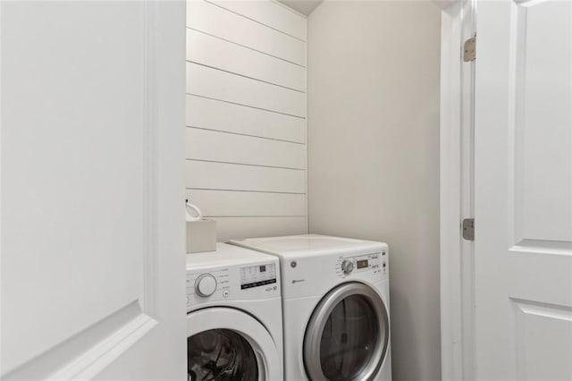 laundry room featuring wooden walls and separate washer and dryer